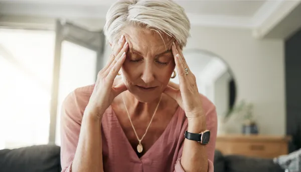 Ältere Frau mit Kopfschmerzen, Stress und Depressionen, während sie sich müde, ausgebrannt und ängstlich auf dem Sofa zu Hause fühlt.